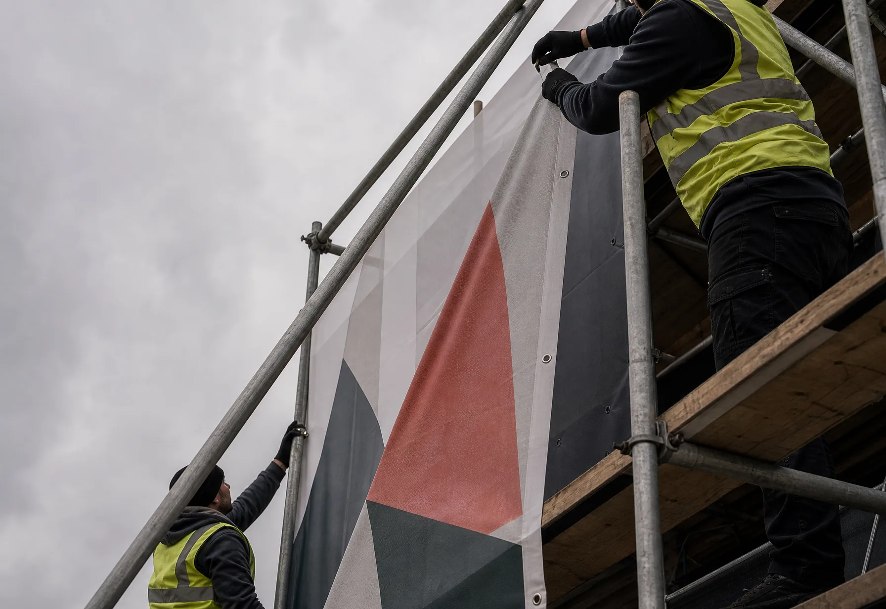 Fitters tensioning a large printed banner onto scaffolding