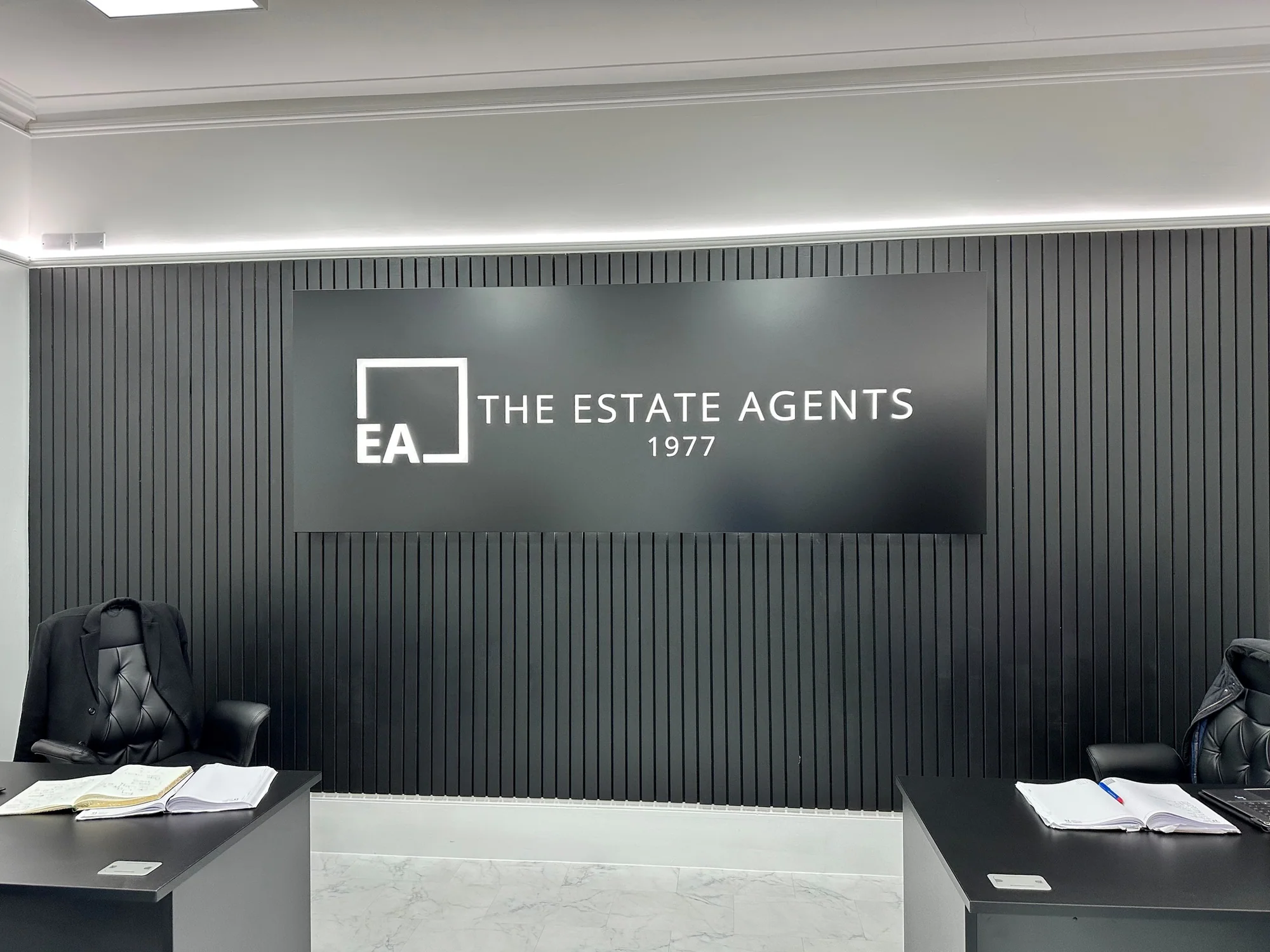 Wide view of The Estate Agents reception wall sign between two desks
